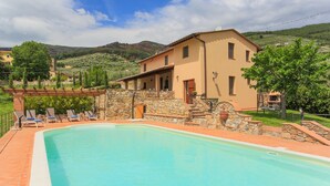 A poolside area with a stone wall, a beige building, and a clear blue sky.