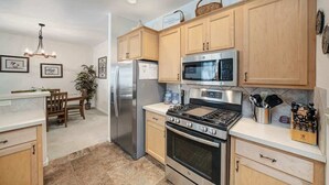 A modern kitchen with wooden cabinets, stainless steel appliances, and a dining area with a chandelier. - Sequoia Pines - 411 Sequoia Circle (Plumas Eureka)