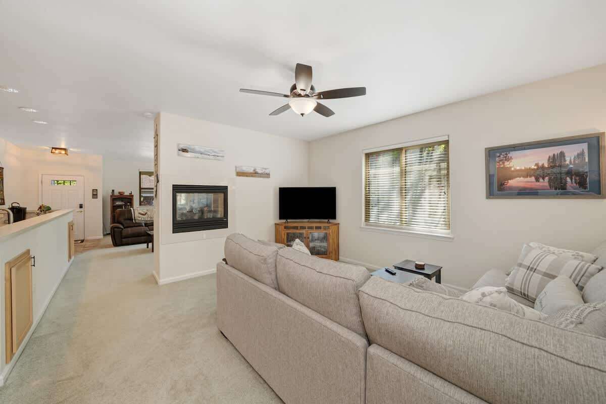 A modern living room with a large sofa, a flat-screen TV, and a ceiling fan.
