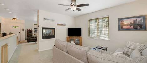 A modern living room with a large sofa, a flat-screen TV, and a ceiling fan.