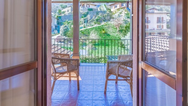 A balcony with wicker chairs, a tiled floor, and a view of houses and greenery.