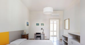 A bedroom with a bed, desk, chair, and a mirror.