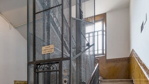 Una escalera con un ascensor metálico y piso de baldosas.