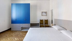 Un dormitorio con una cama grande, un armario azul, dos sillas y una mesita de noche con una lámpara.