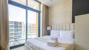 A hotel room with a large window, a bed with white linens, a lamp, and a view of the cityscape. - Nasma Luxury Stays - Riviera 10 (Dubai)