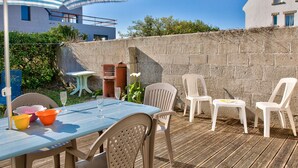 Eine Terrasse im Freien mit Tisch und Stühlen, ein kleiner Tisch mit einer Vase und eine Wand mit einem Fenster.