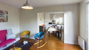 Ein modernes Wohnzimmer mit einer Couch, Sesseln, einem Esstisch und einer Küche im Hintergrund.