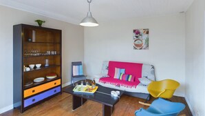 Ein Wohnzimmer mit einer Holzbücherreolen, einem Sofa mit bunten Kissen, einem Couchtisch und einem gelben Sessel.