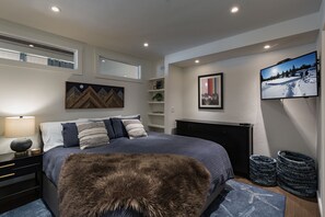 A modern bedroom with a large bed, a fur throw, a TV, and a fireplace. - The Honeycomb | AC, Pool, Hot Tub, Golf & Ski (Durango)