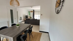 Ein Essbereich mit Holztisch, schwarzen Stühlen und einer Zimmerpflanze. Links befindet sich eine Heizung, rechts eine Uhr.