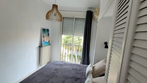 Ein Schlafzimmer mit Bett, Heizkörper, einem Fenster mit Jalousien und einer Pendelleuchte.