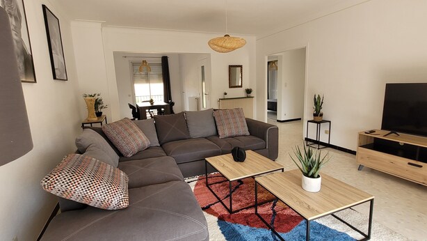Ein modernes Wohnzimmer mit einem Ecksofa, einem Couchtisch, einer TV-Konsole und einem Essbereich im Hintergrund.