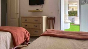 Een slaapkamer met een bed, een dressoir, een televisie en een schuifdeur naar een balkon.
