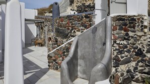 A stone-walled outdoor area with a metal chair, a white door, and a stone staircase. - El Verano Hideaway Villa (Santorini)