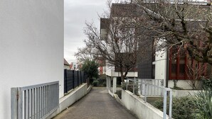 Un callejón estrecho con una verja metálica a un lado y un edificio con un ventanal rojo al otro.
