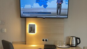 Habitación de hotel con una televisión de pantalla plana mostrando un mapa del tiempo, un escritorio de madera con una computadora portátil, una tetera y vasos.