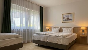 Una habitación de hotel con una cama grande, dos mesitas de noche con lámparas, un cuadro en la pared y cortinas translúcidas.