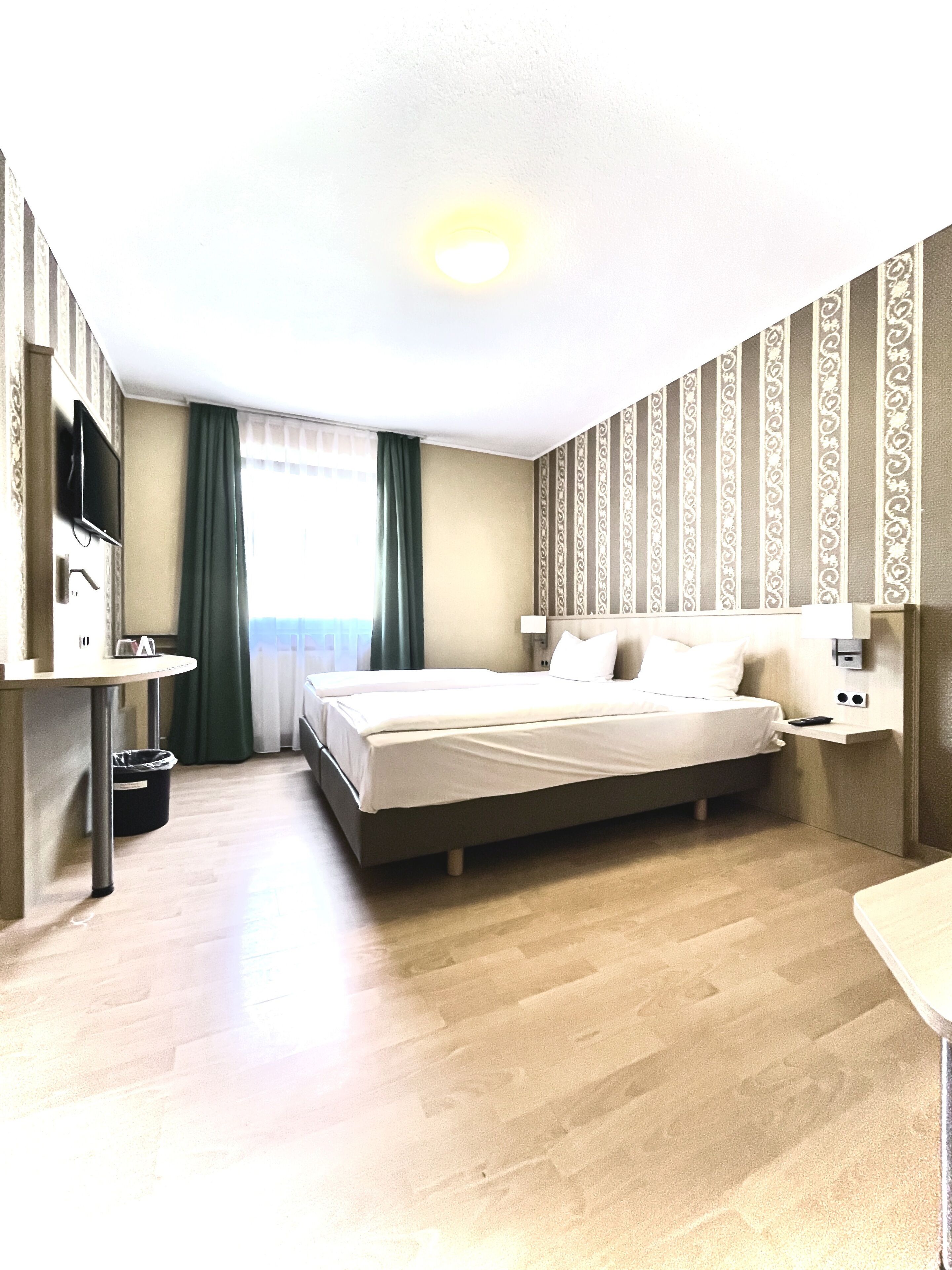 A hotel room with a bed, a desk, a TV, and a view of the sea.