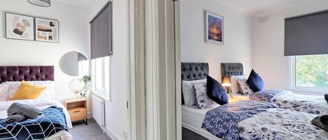 Een slaapkamer met twee bedden, een groot raam en een deur naar een andere kamer.