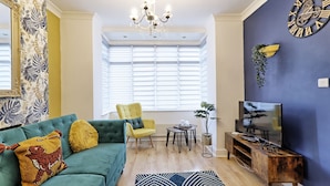 A living room with a green sofa, yellow armchair, and a TV on a wooden stand.