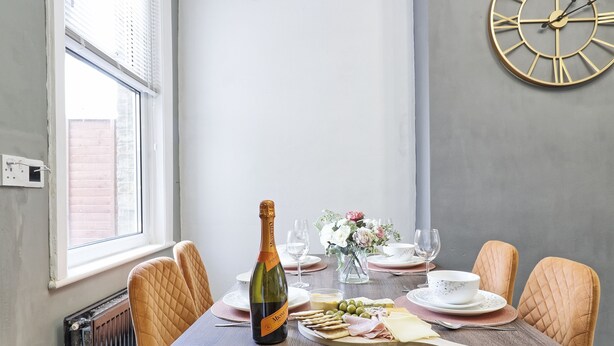 A dining table set with a bottle of champagne, plates, glasses, and a variety of cheeses and olives.