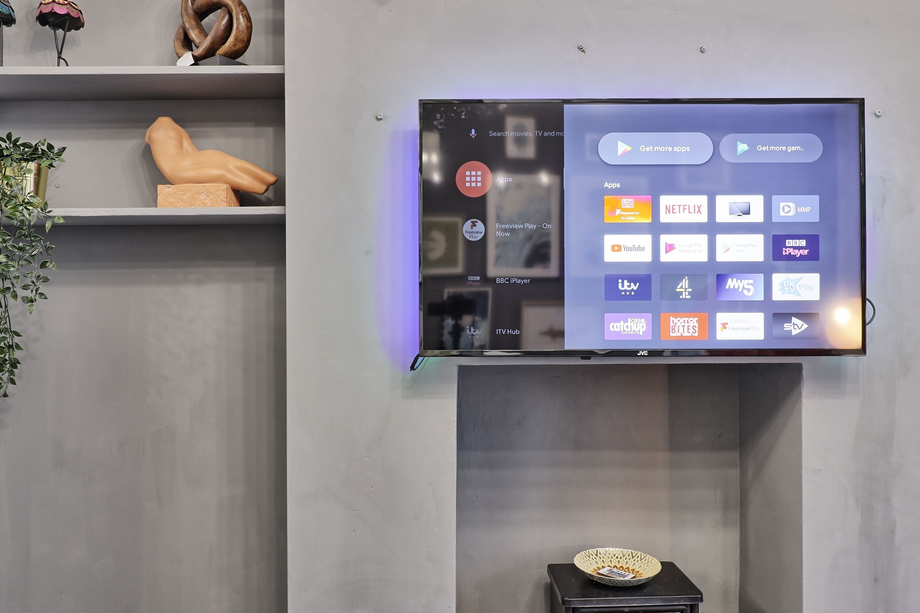 A flat-screen TV mounted on a wall with a selection of streaming apps displayed.