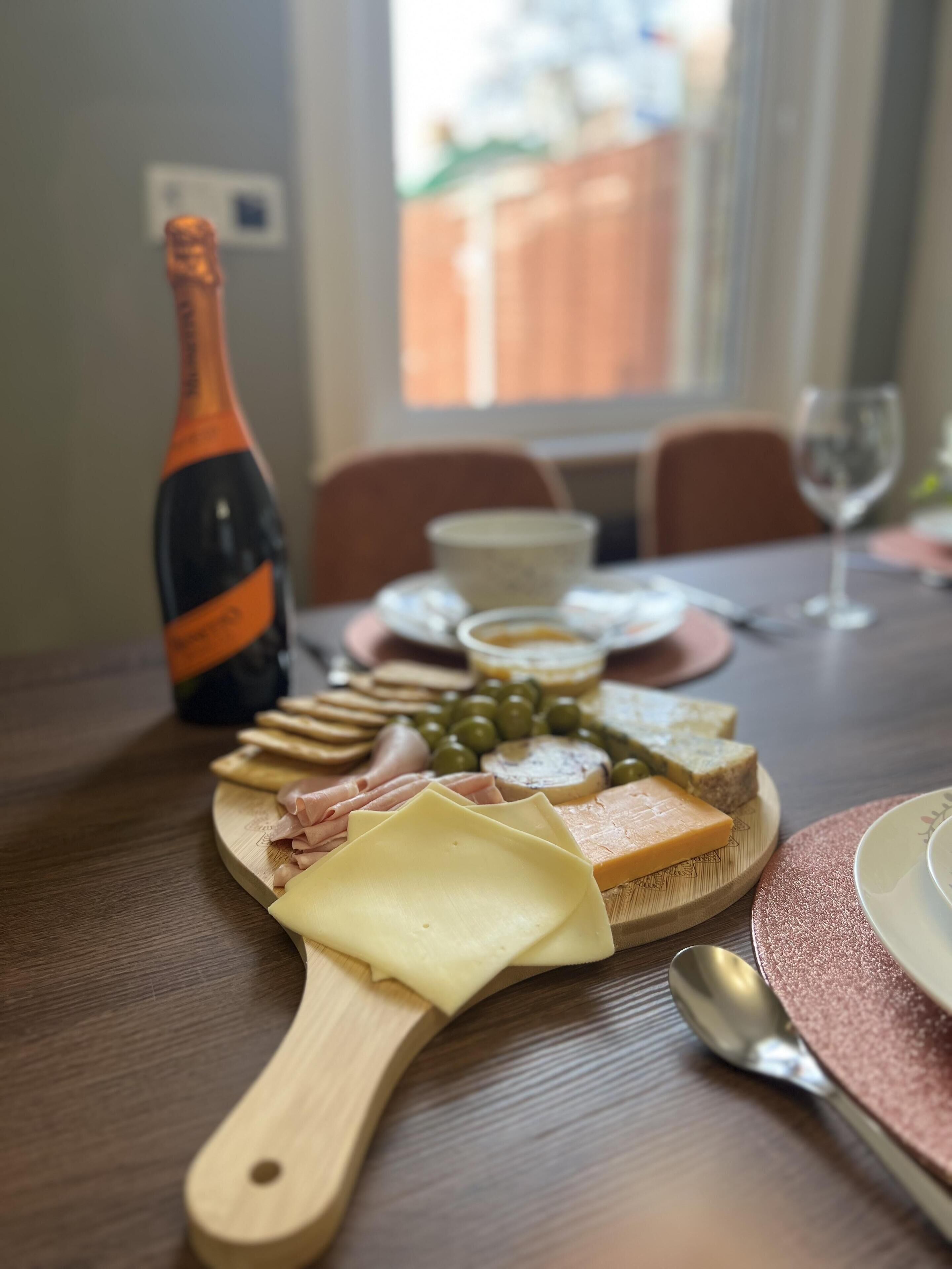A wooden board with various cheeses, olives, and crackers on a table.