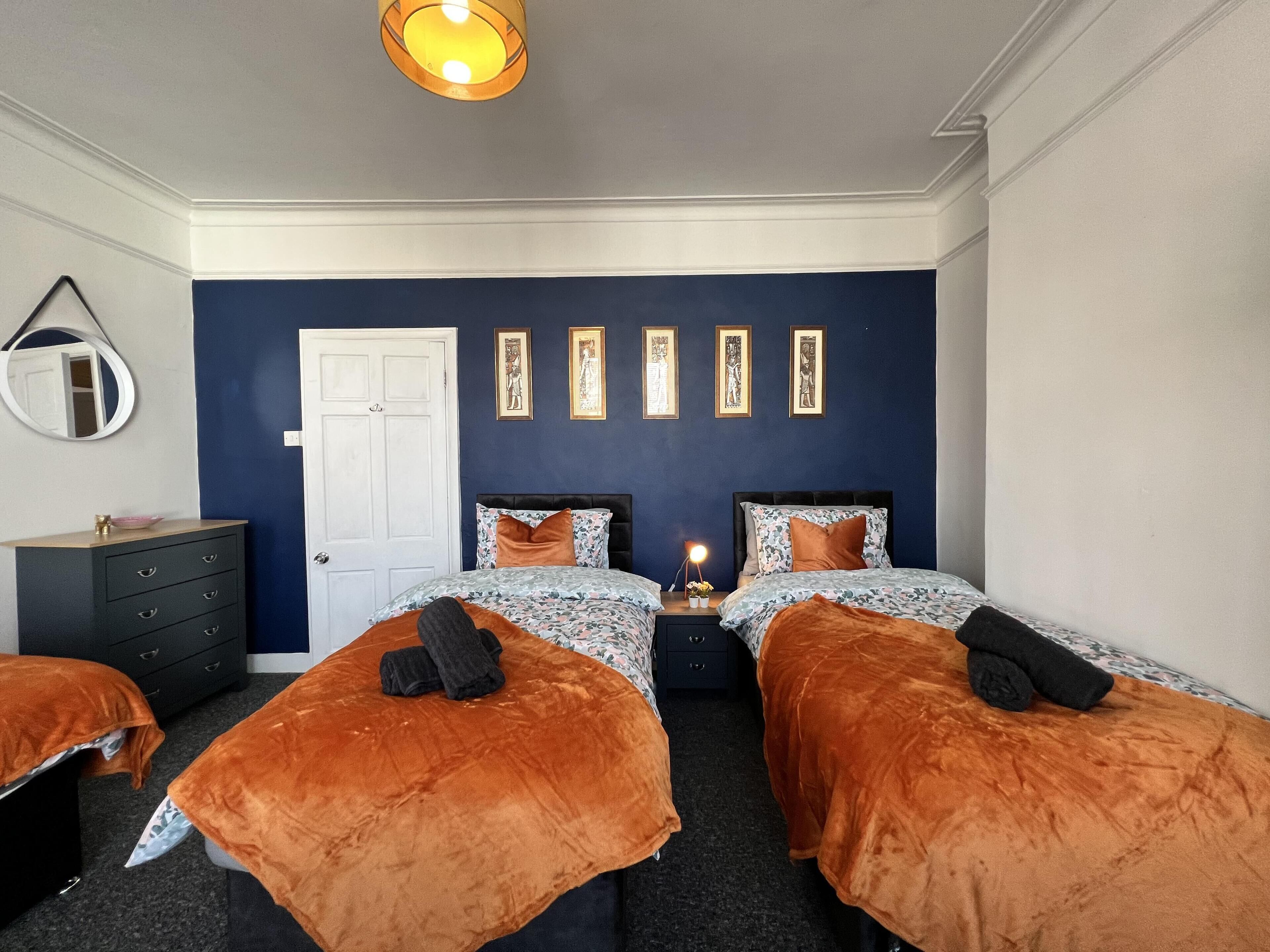 A bedroom with two beds, a dresser, a mirror, and framed artwork on the wall.