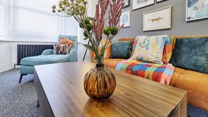 A modern living room with a wooden coffee table, a sofa with colorful cushions, and a vase with flowers.