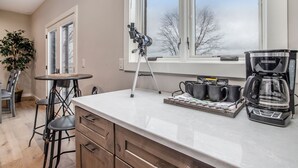 A kitchen with a coffee maker, a tripod, and a window with a view of trees. - Classy Cabin | Beaches | Grand Mere | Wineries (Stevensville)