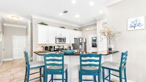 A kitchen with white cabinets, a central island with bar stools, and a decorative plant. - Andrea's Island*Golf Cart*Bikes*BeachSvc+ExtraGear! (DESTIN)