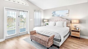 A bedroom with a large bed, a bench, a nightstand with a lamp, and a window with blinds. - Andrea's Island*Golf Cart*Bikes*BeachSvc+ExtraGear! (DESTIN)