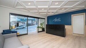 Un área de recepción moderna con un muro de cristal, una mesa de recepción y una zona de estar.