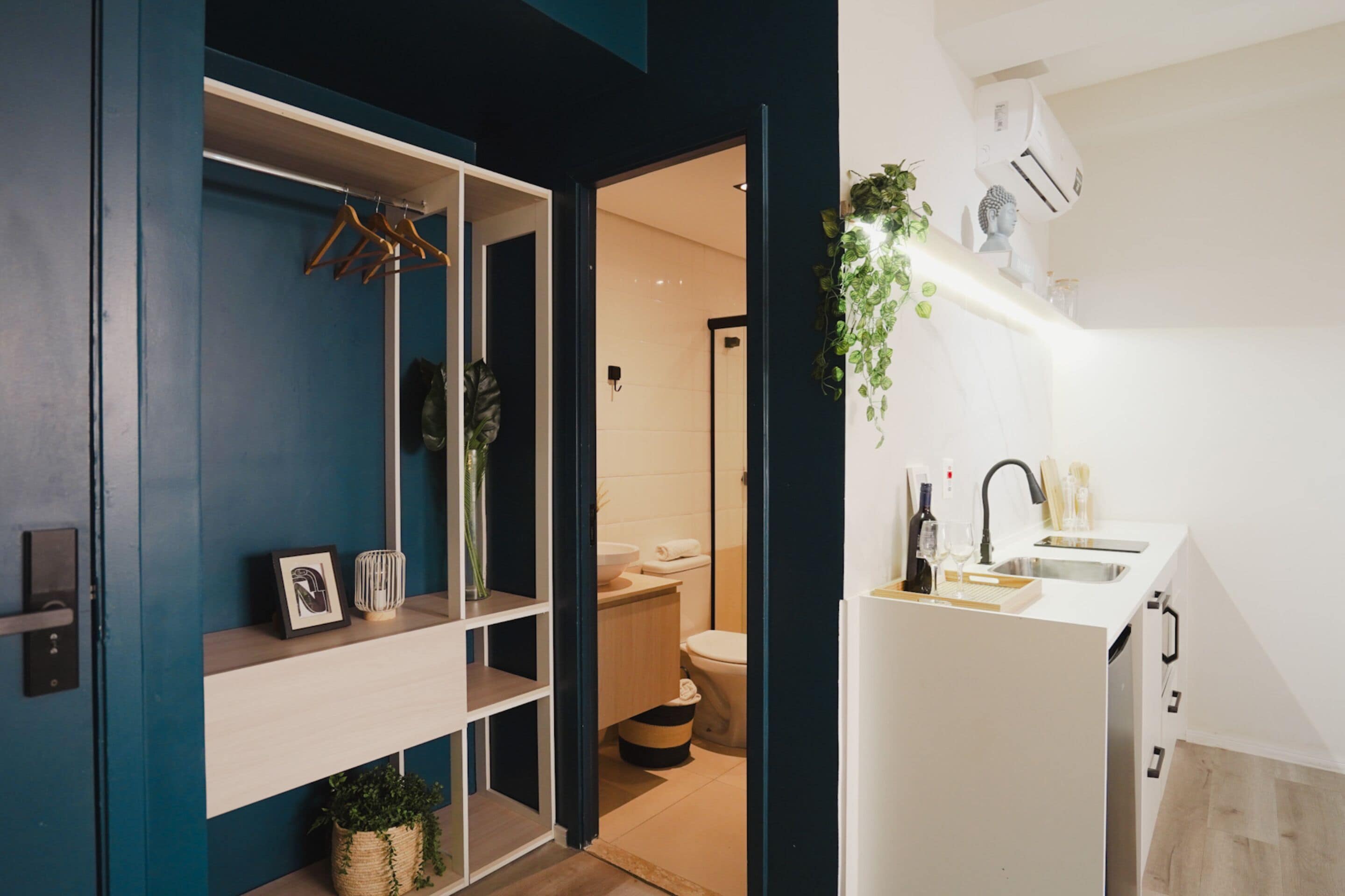 Une salle de bain moderne équipée de toilettes, d’un lavabo et d’une douche. On y trouve une étagère avec des serviettes et une plante suspendue.