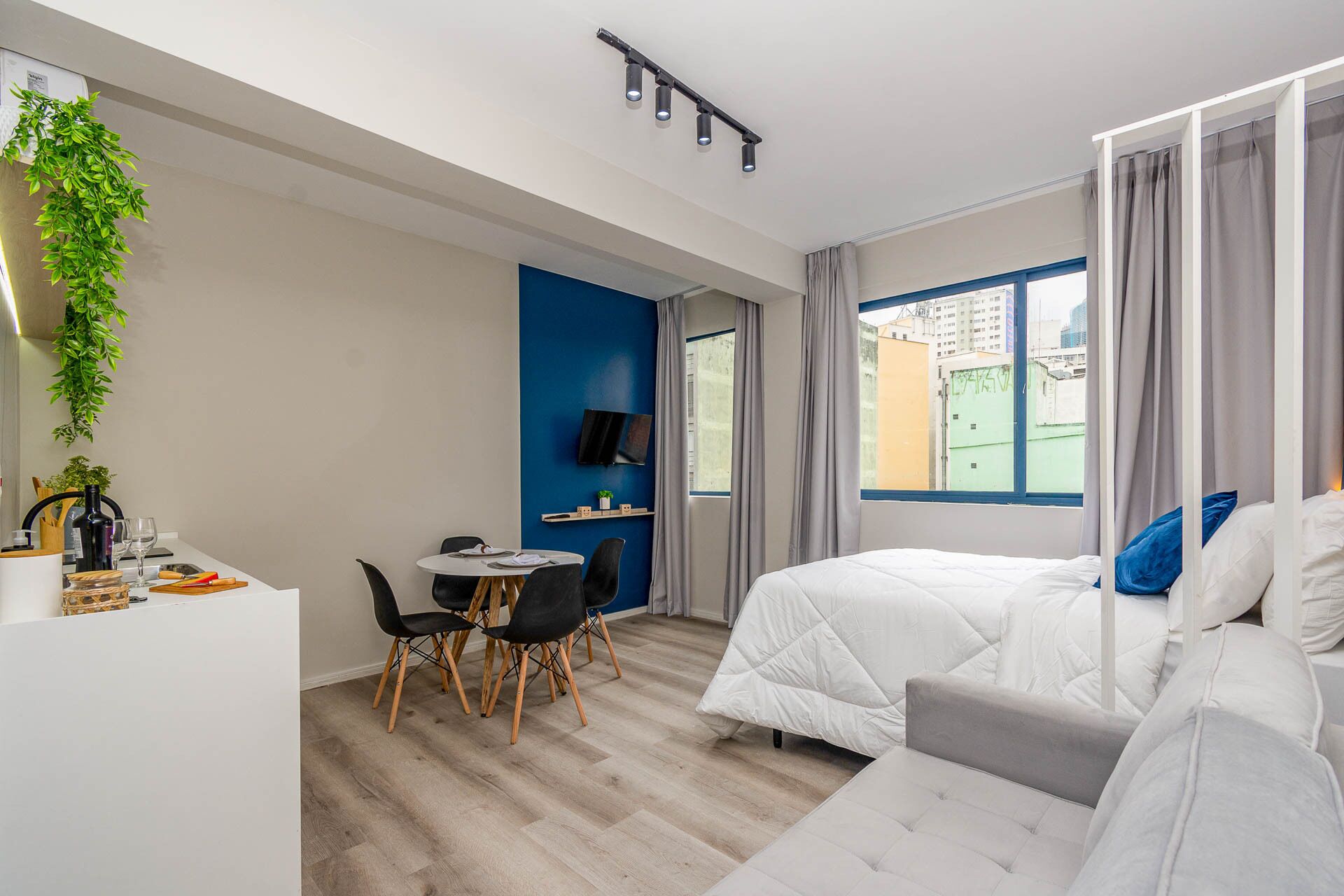 A modern hotel room with a bed, a desk with a chair, a TV, and a window with curtains.