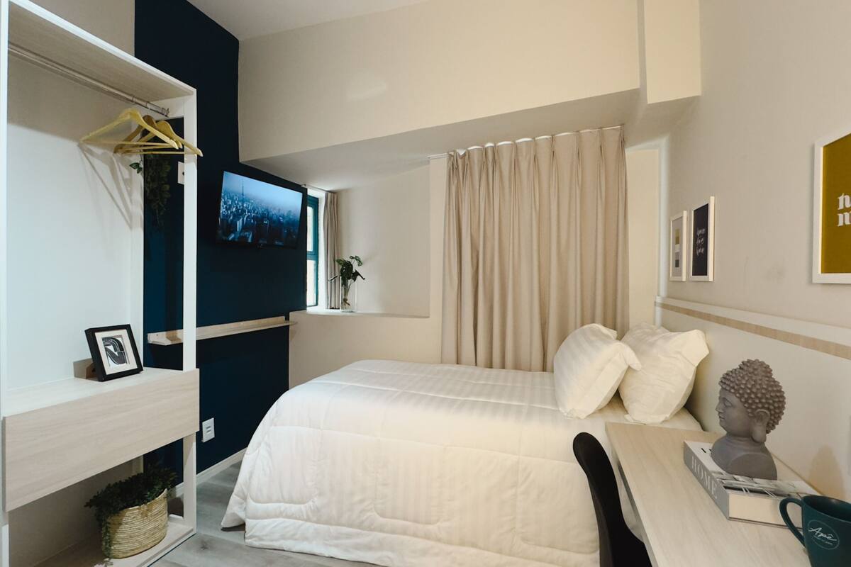 Une chambre d’hôtel bien rangée, avec un lit, un bureau, une télévision et une statue de Bouddha.