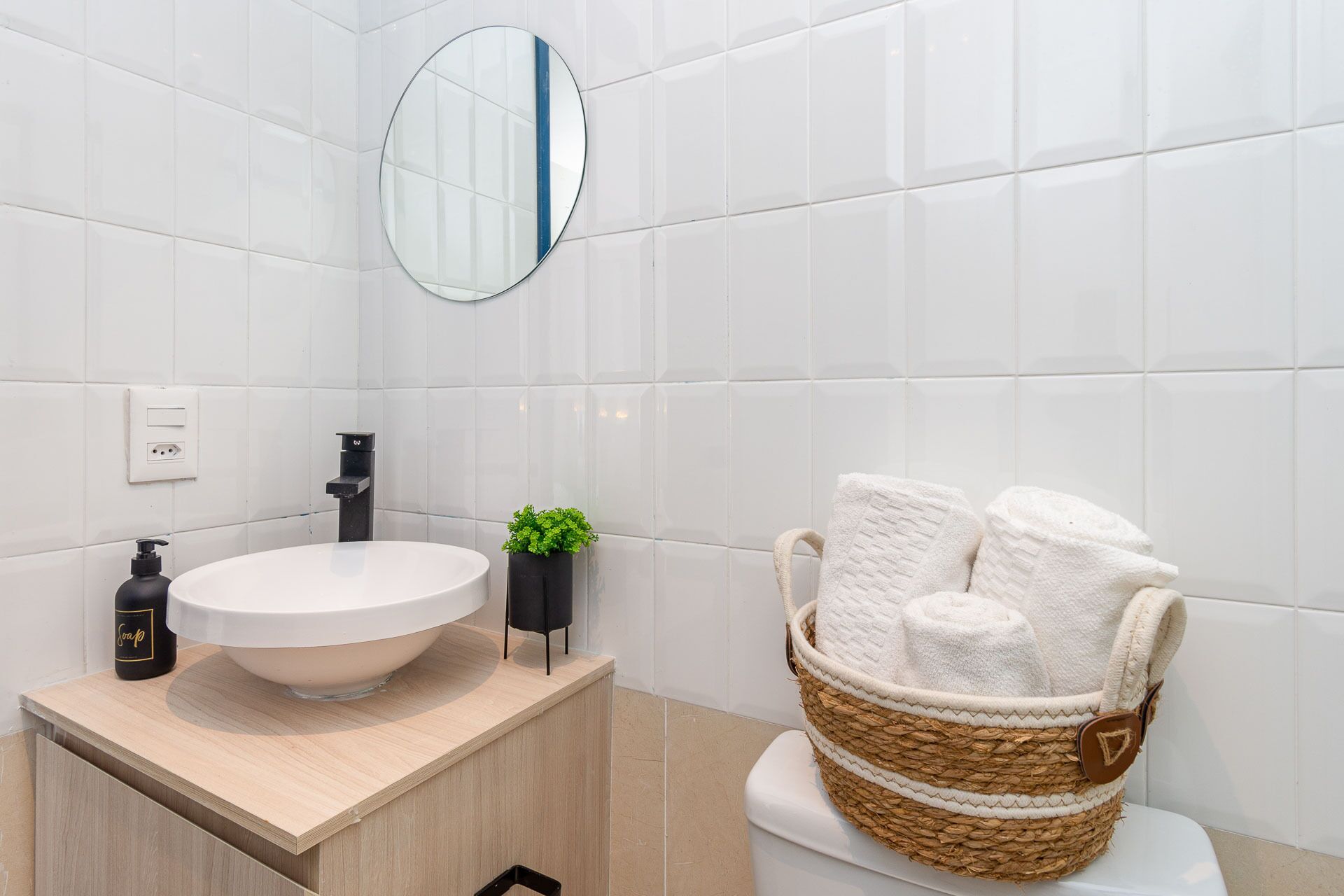 Un baño moderno con un lavabo blanco, un espejo redondo y una cesta de mimbre con toallas.