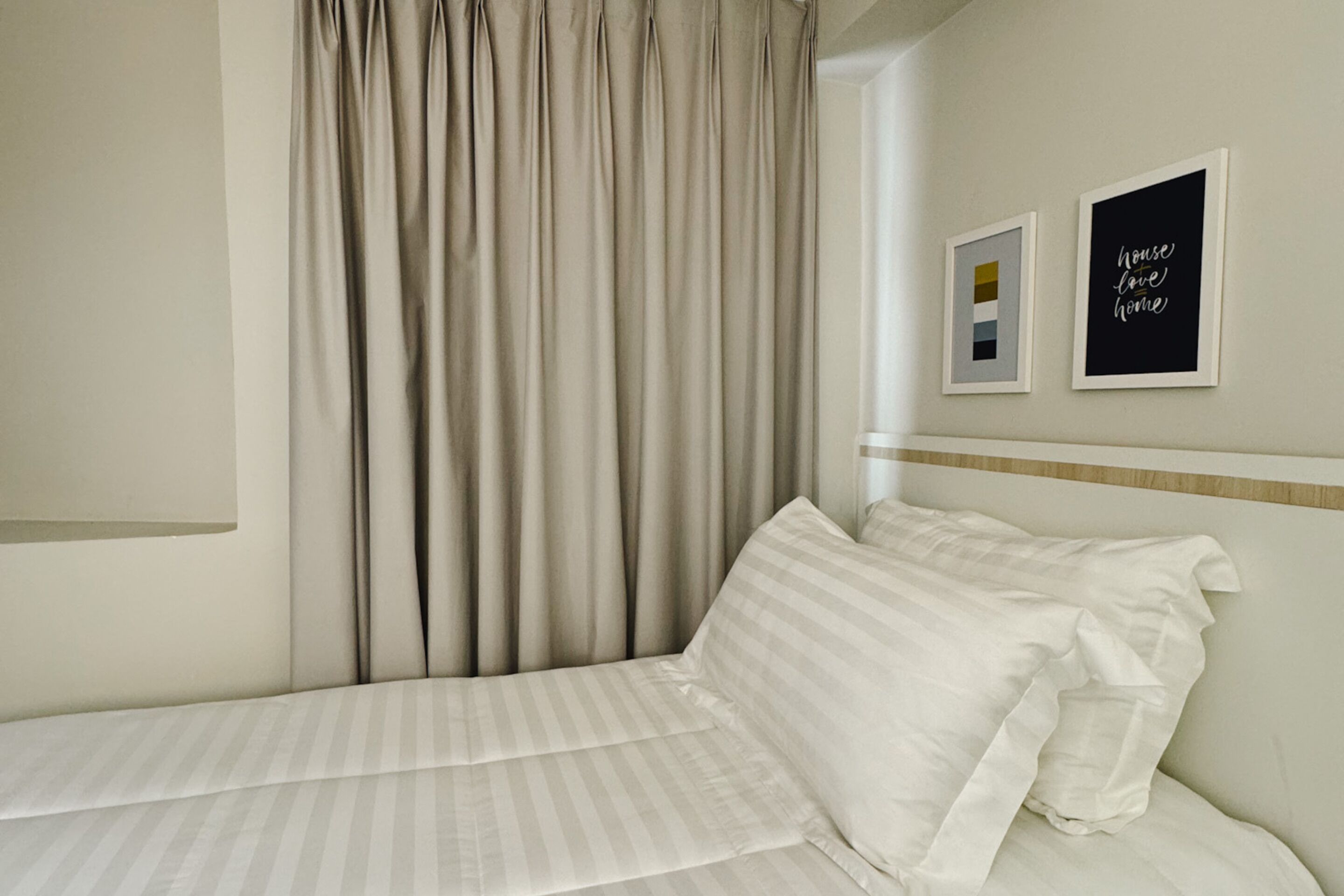 A neatly made bed with white linens, a headboard with a wooden trim, and two framed pictures on the wall.