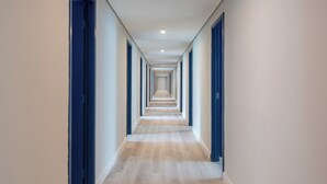 Un largo pasillo estrecho con piso de madera y puertas azules a ambos lados.