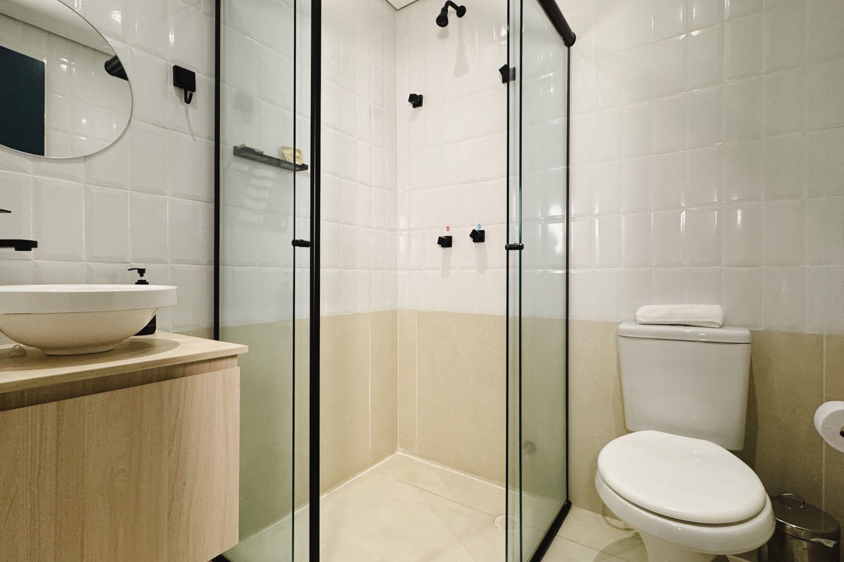 Un bany modern amb plat de dutxa de vidre, un vàter i un lavabo amb un mirall a sobre.