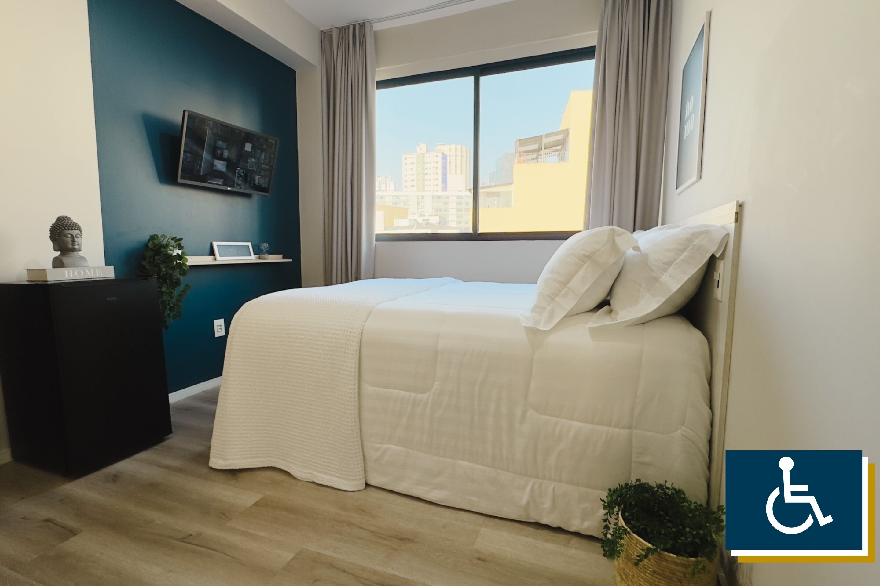 Habitación de hotel con cama, escritorio, televisión y ventana con vistas a la ciudad.