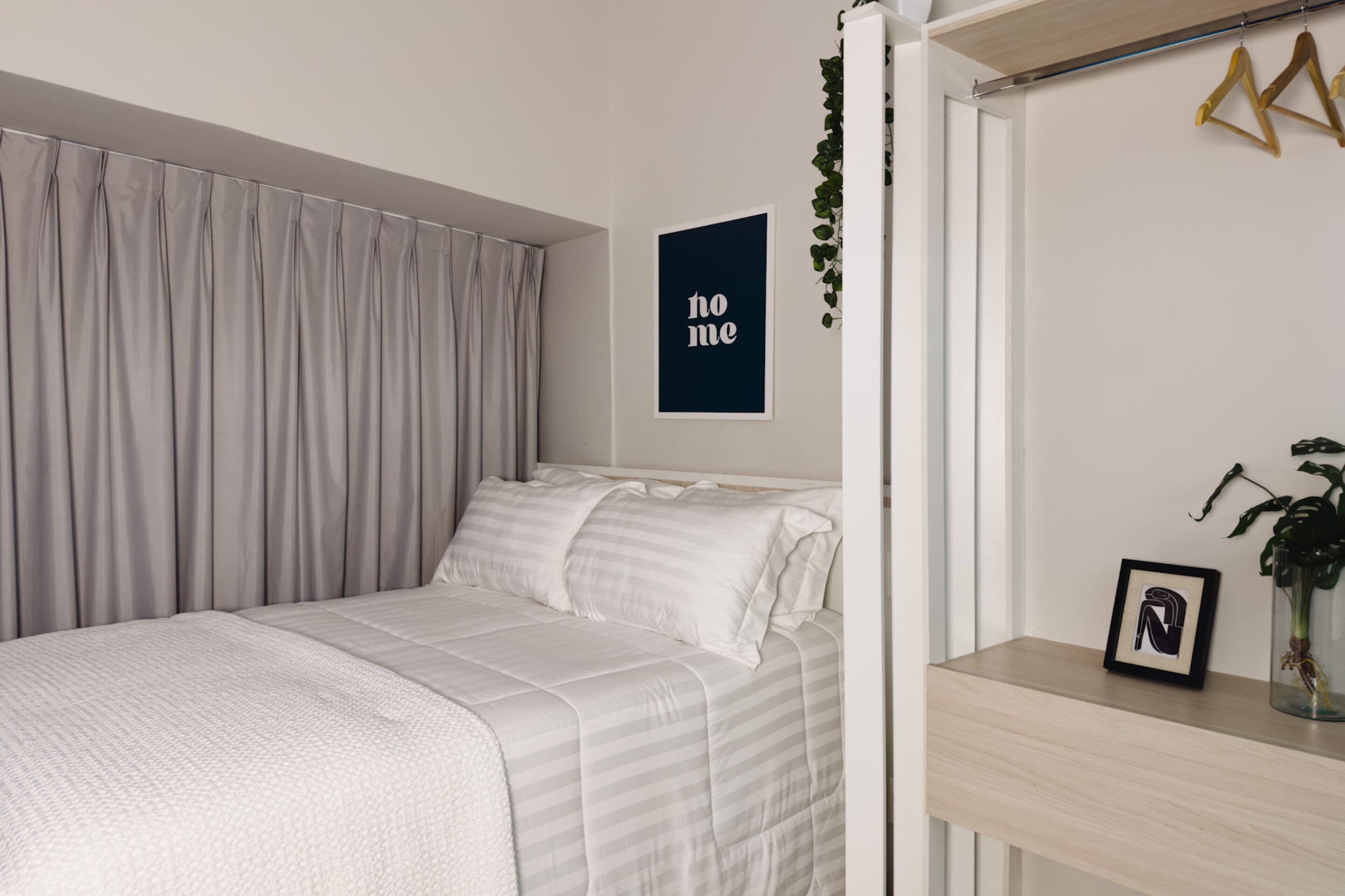 A neatly made bed with a striped duvet, a framed picture on a bedside table, and a 'home' sign on the wall.