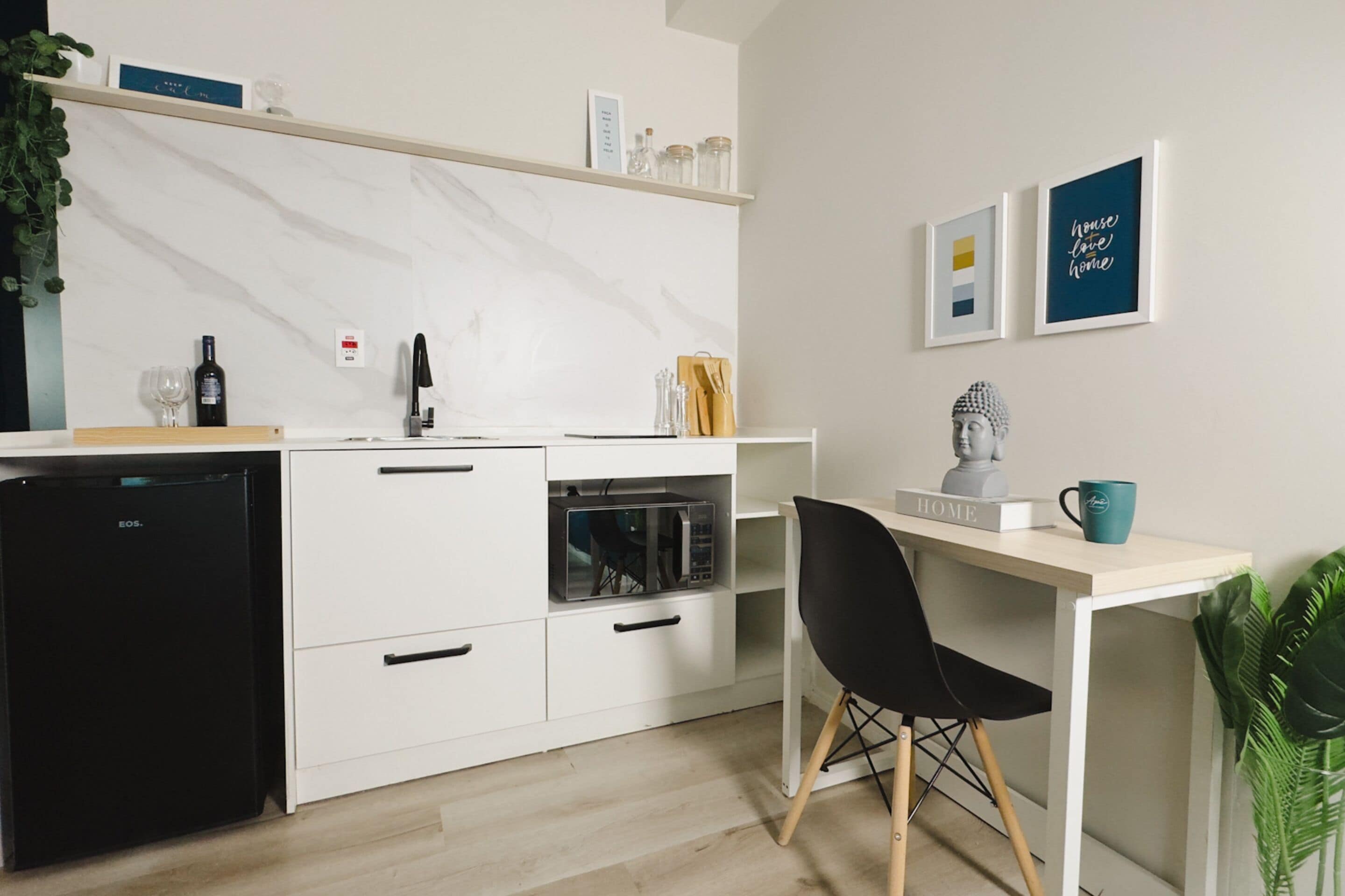 A modern kitchen with white cabinets, a black refrigerator, and a wooden countertop. There is a black chair and a small table with a blue mug.