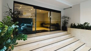 Un interior moderno con una puerta de vidrio que da a una sala de estar, una escalera y plantas en macetas.