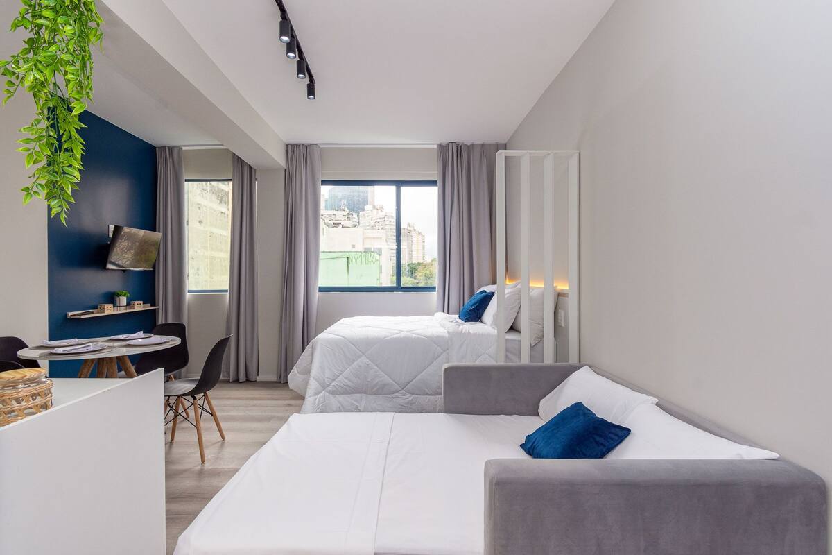 Une chambre d’hôtel avec deux lits, un bureau avec une chaise, une petite table et une grande fenêtre donnant sur la ville.
