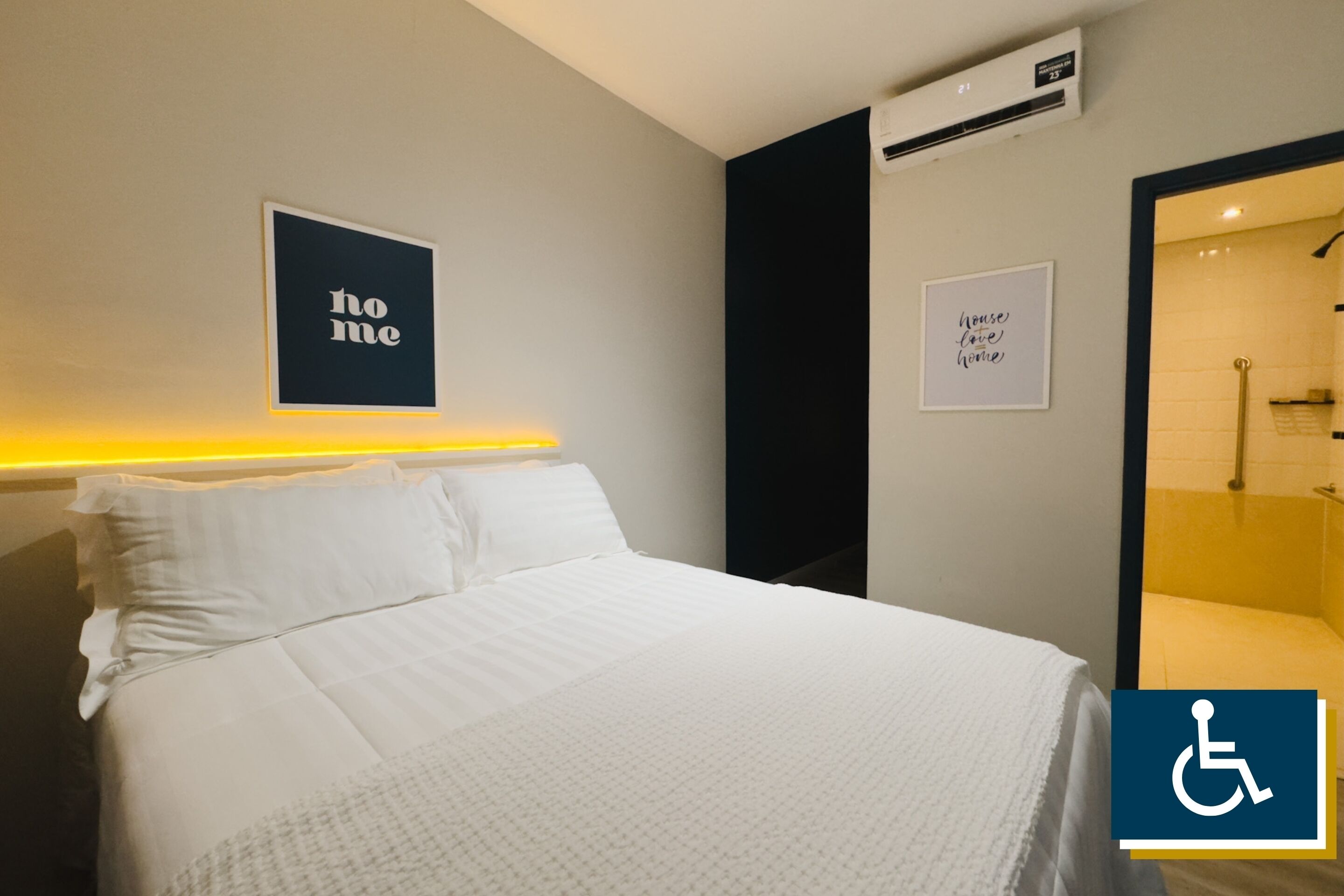 Quarto de hotel com cama, ar condicionado fixado na parede e um letreiro com a palavra 'home'.