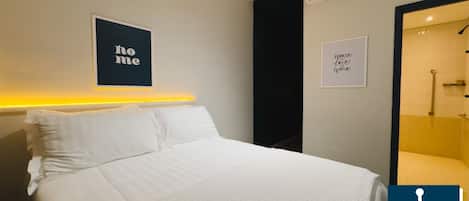 Quarto de hotel com cama, ar condicionado fixado na parede e um letreiro com a palavra 'home'.