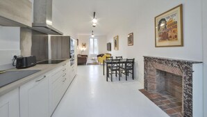 A modern kitchen with white cabinets, a built-in stove, and a dining area with a fireplace. - Appartment the House of Hera (Vierzon)