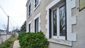 A two-story building with white-framed windows and a small green bush in front. - Appartment the House of Hera (Vierzon)