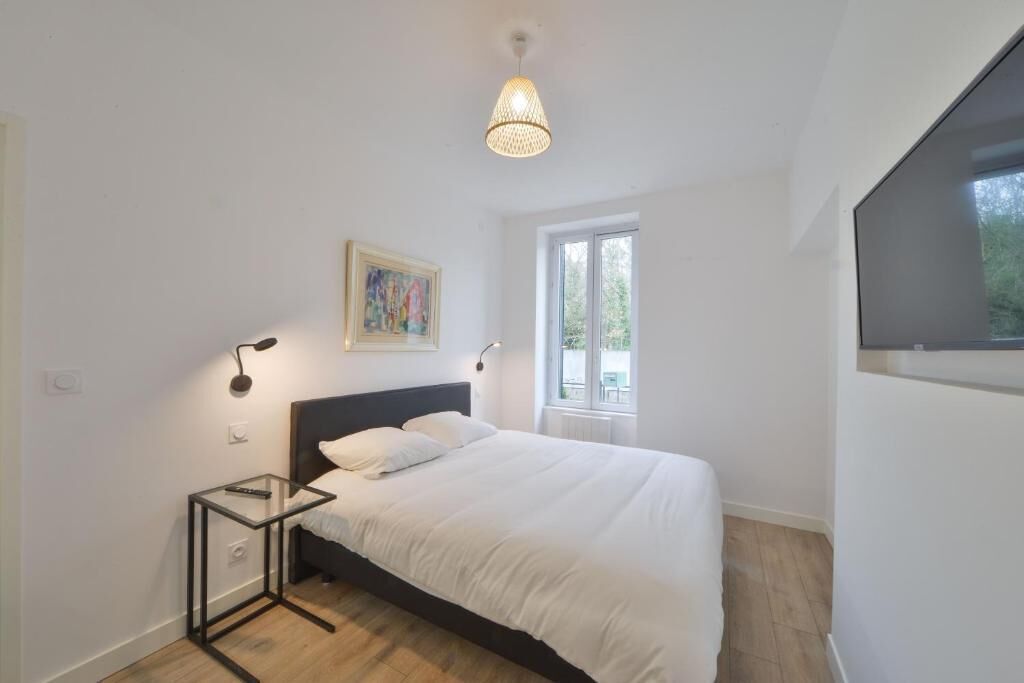 Quarto moderno com cama, mesas de cabeceira, luminária pendente, janela e uma pintura na parede.